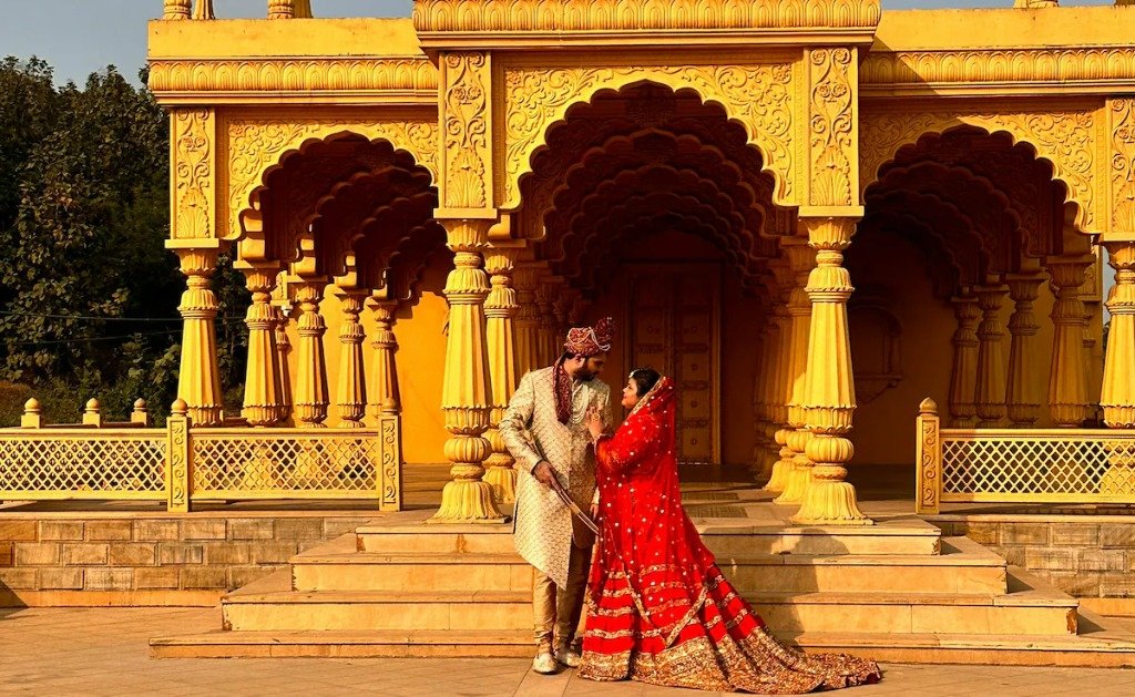 Couple in red and gold outfits posing in front of yellow palace structure