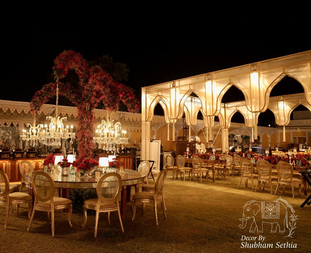 Elegant outdoor dinner setup with crystal chandeliers and red floral arches by Decor by Shubham